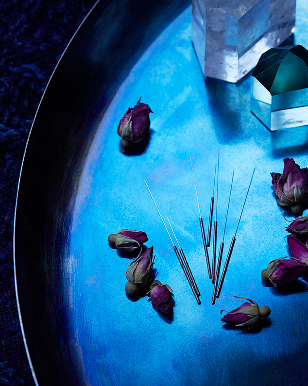 Acupuncture needles on blue metal tray with flowers and crystal